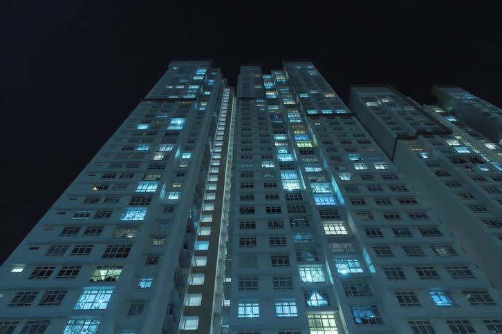 Looking up at skyscrapers with window lights flickering day to night transition