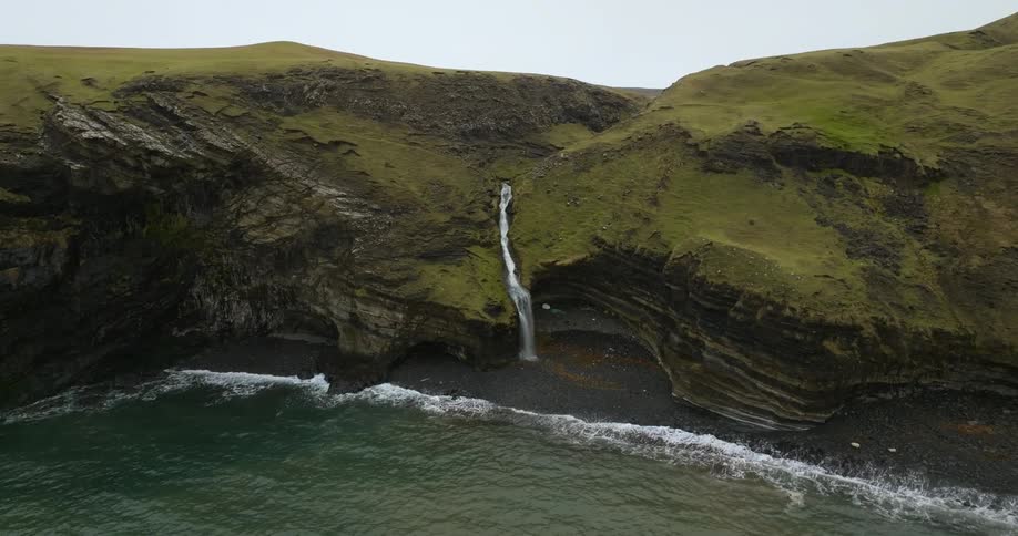 Aerial view of a waterfall flowing down the slopes of a mountain into the ocean
