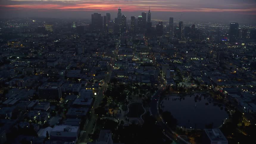 Aerial shot tilting up from MacArthur Park to reveal the downtown Los Angeles skyline at sunrise during winter
