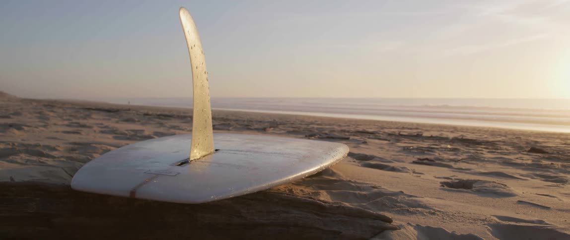A surfboard is lying on the sand on the beach as waves roll in to shore