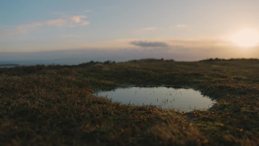 A hole with water in it is in the grass with a blue sky behind it