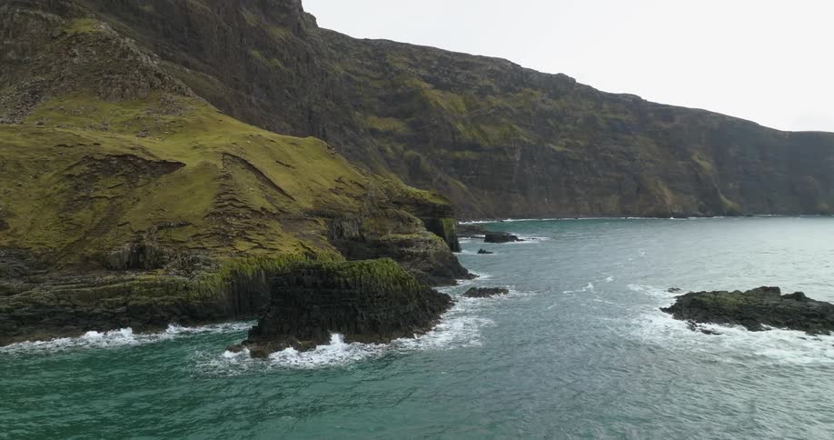 Waves crash against moss covered cliffs on misty day