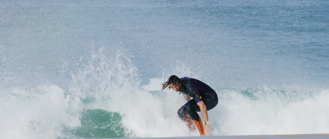 Young man wearing a wetsuit rides a surfboard on a wave in the coast at daytime