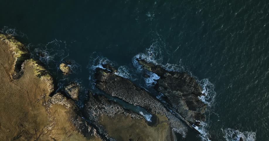 Aerial view of cliff overhanging pacific ocean with light waves at high tide