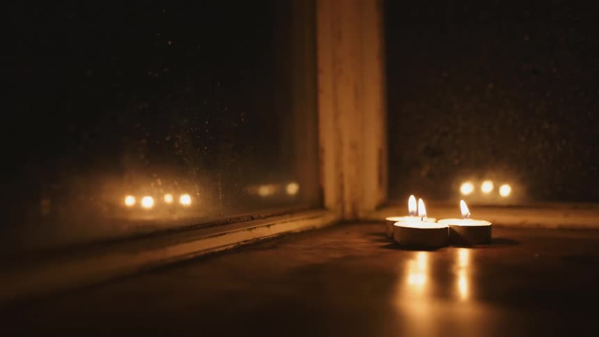 Three burning tea candles next to a window at night