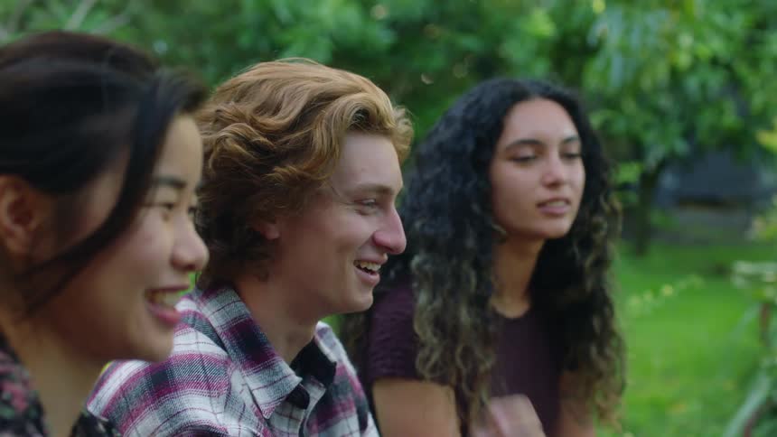 Friends sitting outdoors near lawn smile and laugh together as they talk