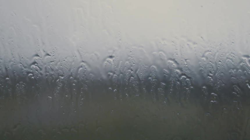 Rain falls on a foggy window and trickles down the glass