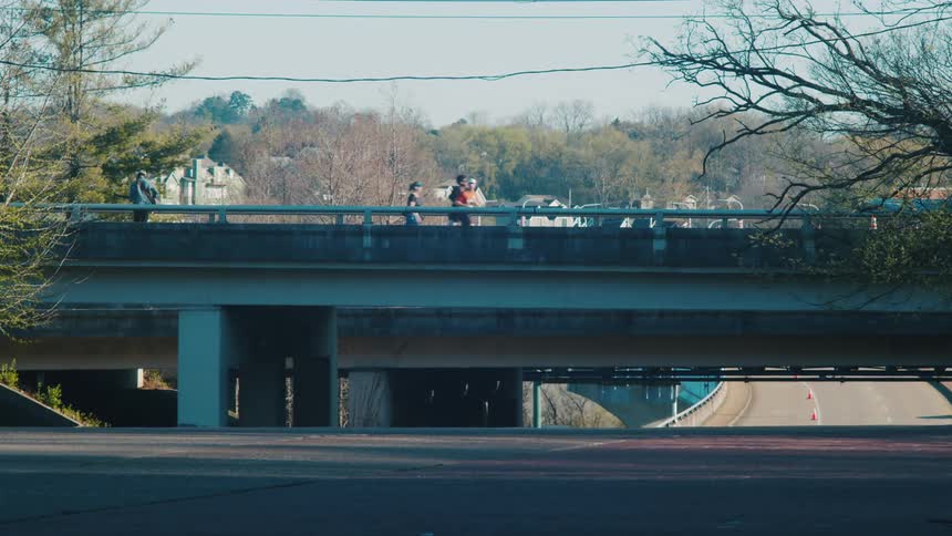 A group of people jogs over a bridge near traffic on a small town at morning