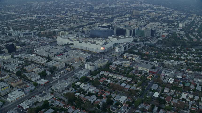 Aerial footage at sunrise over Beverly Hills California approaching Beverly Center and Cedars-Sinai Medical Center through residential mansions and cloudy skies