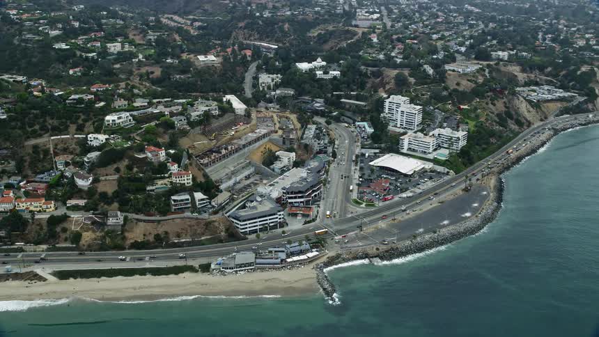 Morning traffic flows on a coastal highway as it meets Sunset Boulevard in Pacific Palisades California with residential areas and cloudy skies visible in the distance