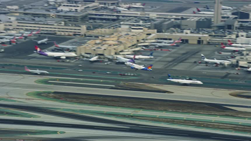 A commercial airliner takes off from LAX in the morning captured in aerial stock footage during summer