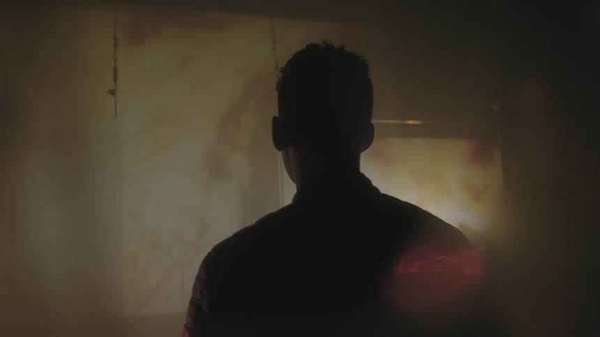 A man looks at a projection of fire on the wall