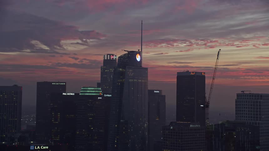 Aerial footage at sunrise of the Wilshire Grand Center in Downtown Los Angeles with cloudy skies and the citys other skyscrapers visible in the background during winter