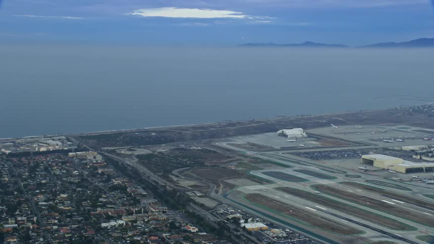 An aerial shot captures a plane taking off from LAX during sunrise with the city of Los Angeles visible in the background
