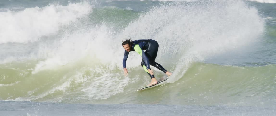 A man wearing a wetsuit is surfing and riding wild waves as the water splashes around him