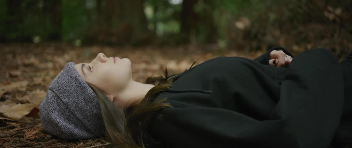 Woman wearing knit hat lies on ground in forest among fallen leaves