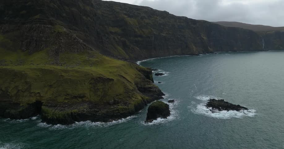 Waves crash against islets andbase of cliff on misty day under an overcast sky