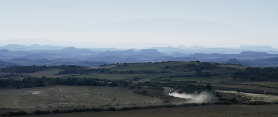 A car traveling on a dirt road and kicking up dust in a rural area