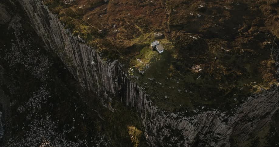 A small hut purched ontop of a coastal cliff with rugged terrain