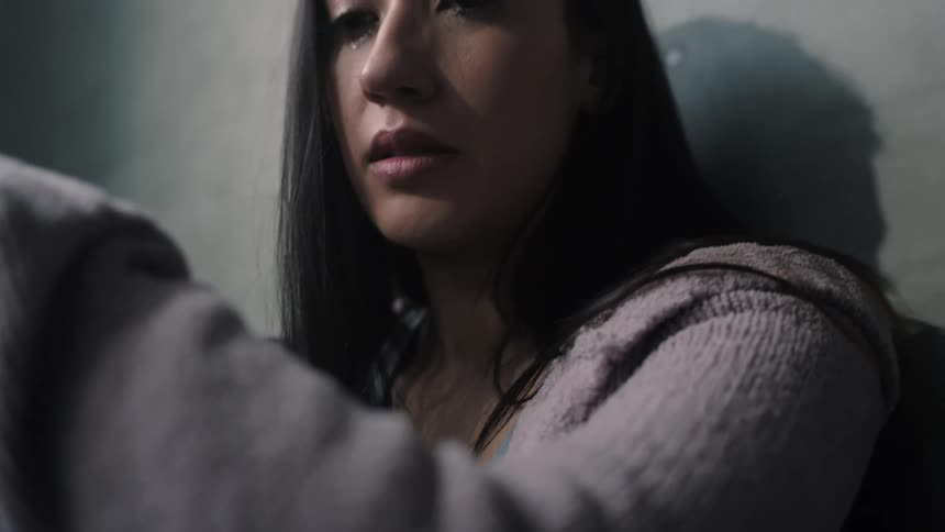 A sad woman wearing leggings sits with her knees pulled into her chest while crying