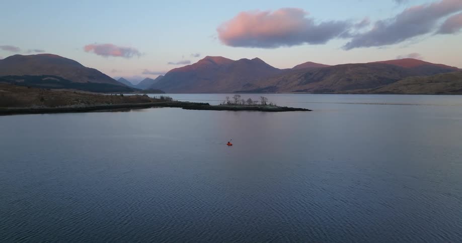 Person paddles across lake with red tinted clouds and mountains in the background