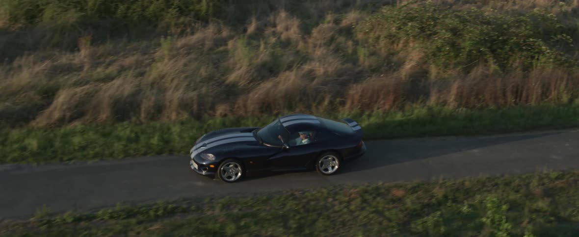 A black sports car with white stripes is traveling on a rural road through farmland