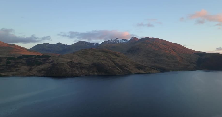 Red tinted clouds sit in sky over mountains and shore