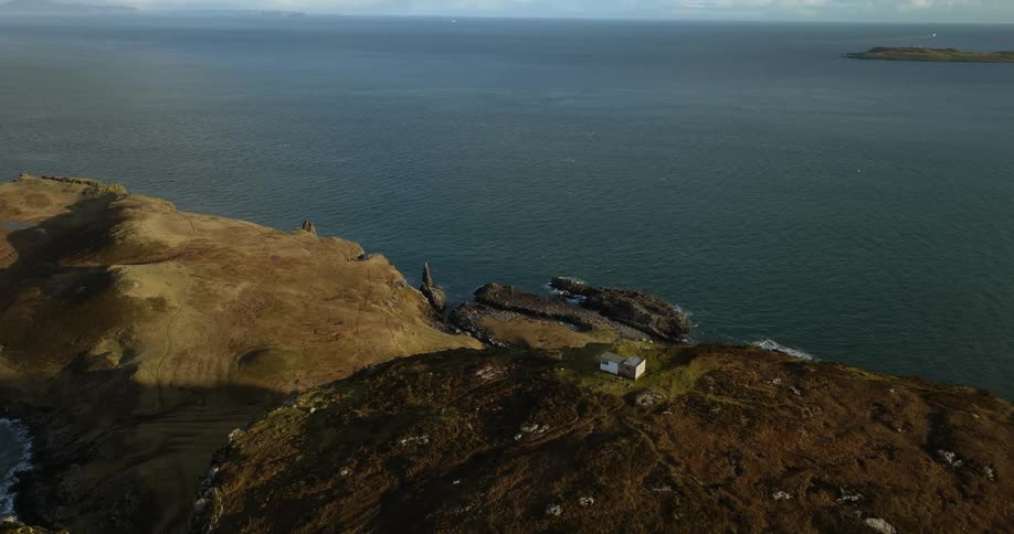 Lone building sits on hill overlooking ocean as birds fly nearby