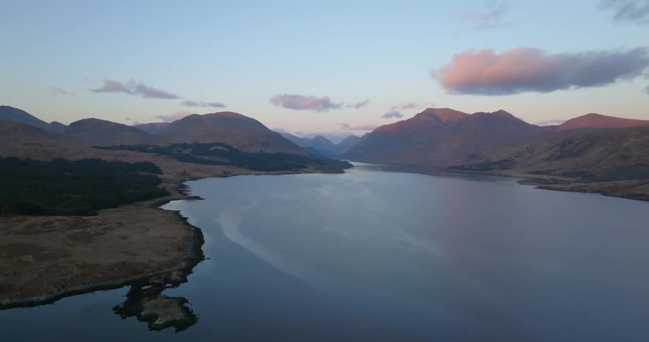 Aerial view of the calm surface of a lake next to the mountains at evening