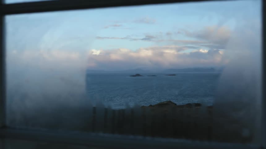 Small islands in the ocean seen in the distance through the foggy glass of a window at morning