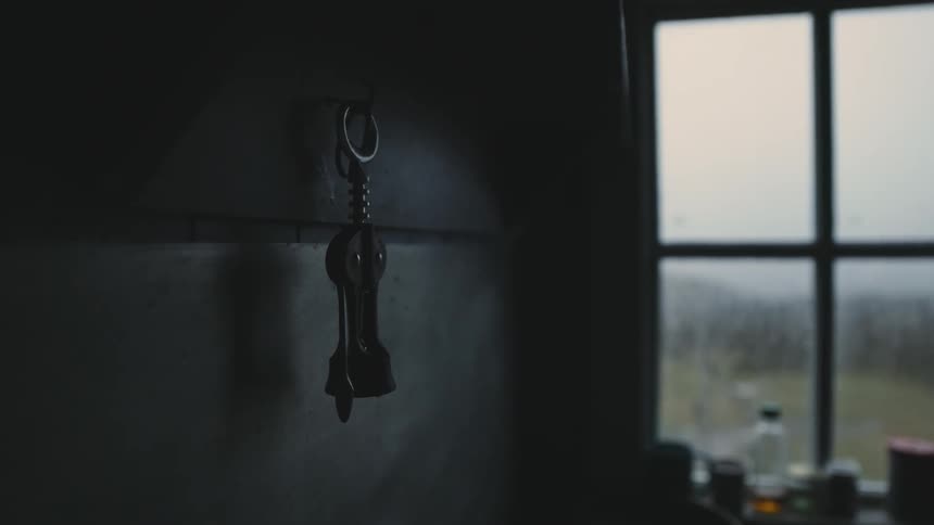 A tool is hanging on a wall with a single hook on it near a window with bottles on the windowsill