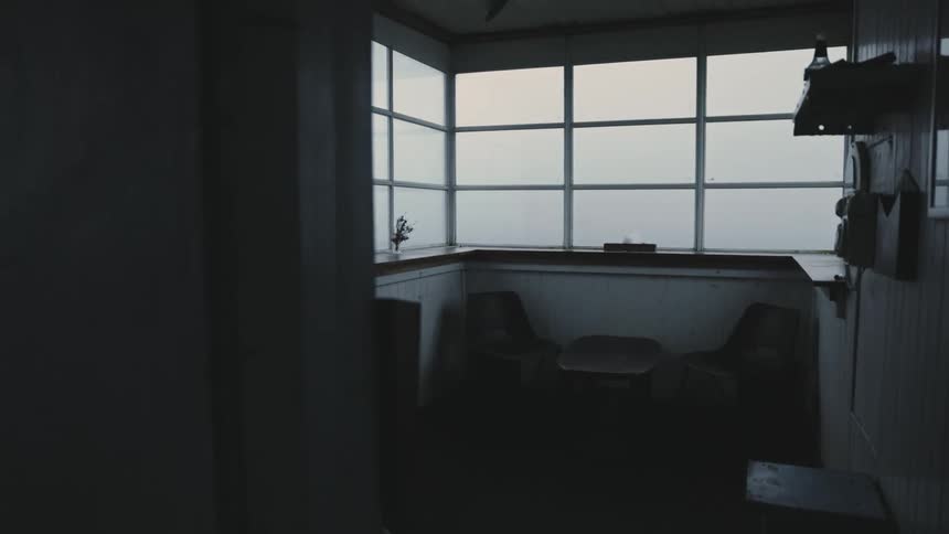 A small table with two chairs is shown in a black and white interior scene with a big window behind it and some things hanging on the wall