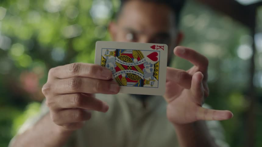 Man turns a king of hearts into an ace of spades outdoors during a magic trick