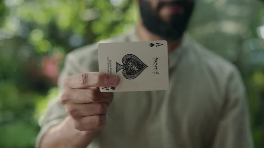 A young bearded magician does magic tricks with cards on the garden
