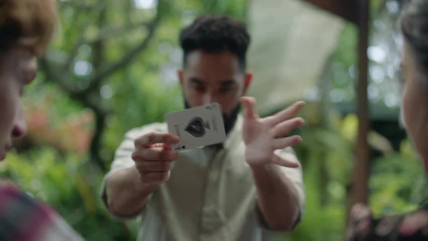 A man holding a card out in front of two others and then he flicks the card and the card changes face