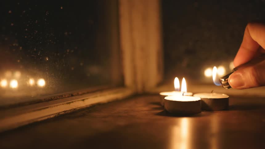 Nearby windows reflect flames on candles after they are lit by person at night