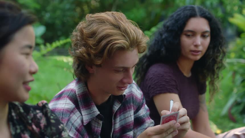 A young man smiles as he writes on a playing card with a marker during an outdoor magic show