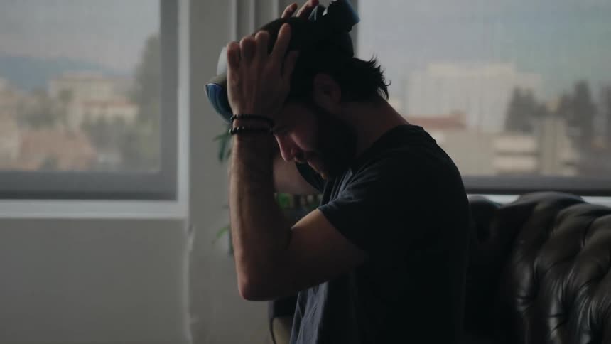 A man sitting in his living room puts a virtual reality headset on his head