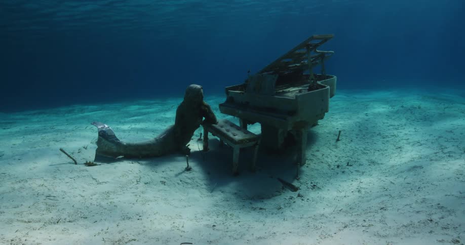 A statue next to a piano in the ocean is displayed
