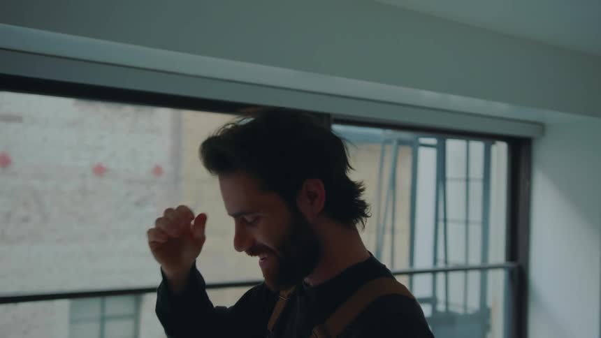 A man is standing near windows wearing a virtual reality headset as he takes it off and rubs his hand across his head with a smile on his face