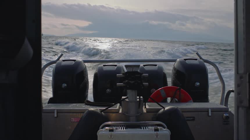 Open doorway shows motorboat speeding across ocean leaving a wake on a cloudy day