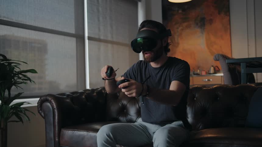 A man using a virtual reality headset while sitting on a leather sofa at home