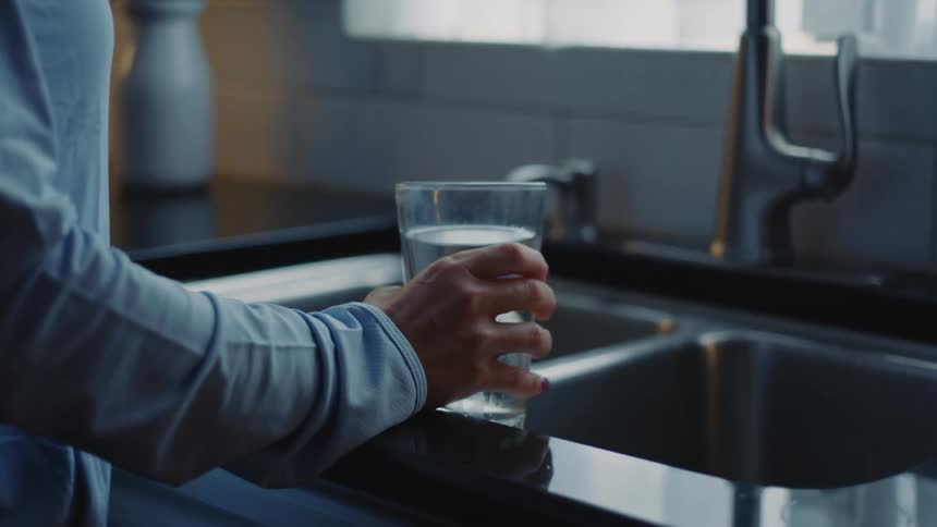 Woman stands in front of clean kitchen sink holding a glass filled with water