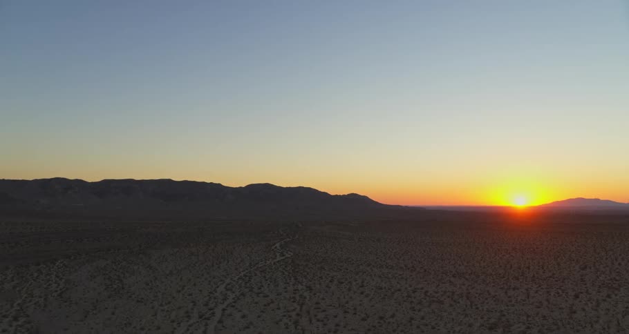 An aerial view of a sun setting on a desert horizon with mountain silhouettes
