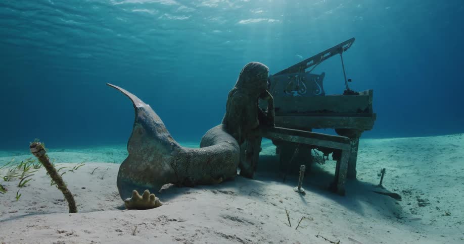 A statue of a woman sits next to a piano underwater