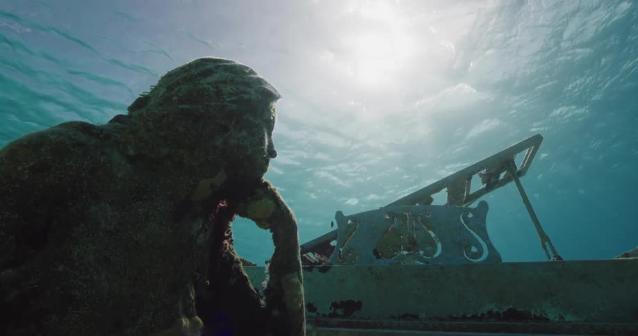 A female statue and piano underwater with sun shining through the surface