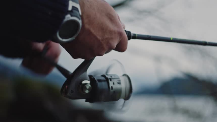 A close up of a persons hand reeling a fishing pole wearing a wristwatch