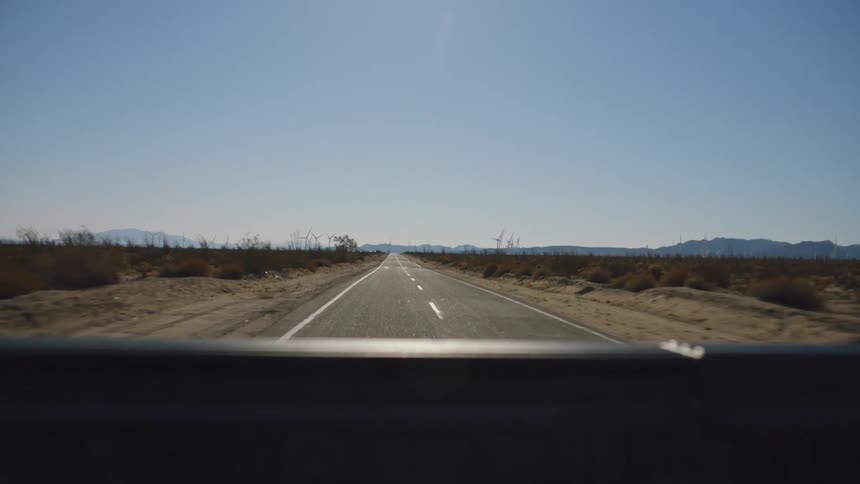 Traveling on a rural desert road with plants and vegetation and mountains in the distance under a clear sky