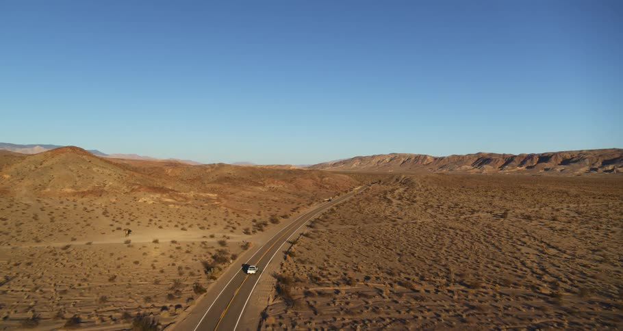 A car drives down the highway in the desert