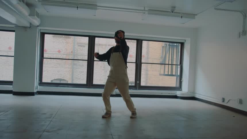 Man with beard and white overalls and shoes uses vr headset with motion controllers in building